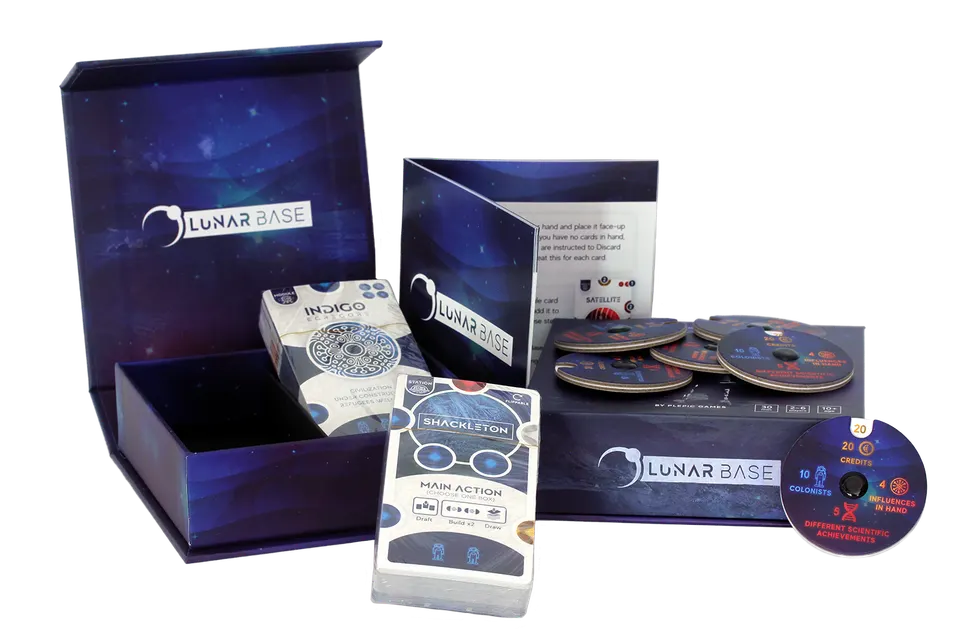 The Lunar Base box open on a plain background, its lid raised behind the empty tray, with a squared stack of cards topped by the Shackleton main-action card, a small card tuck box, the rulebook standing open, and several round scoring discs arranged in front.